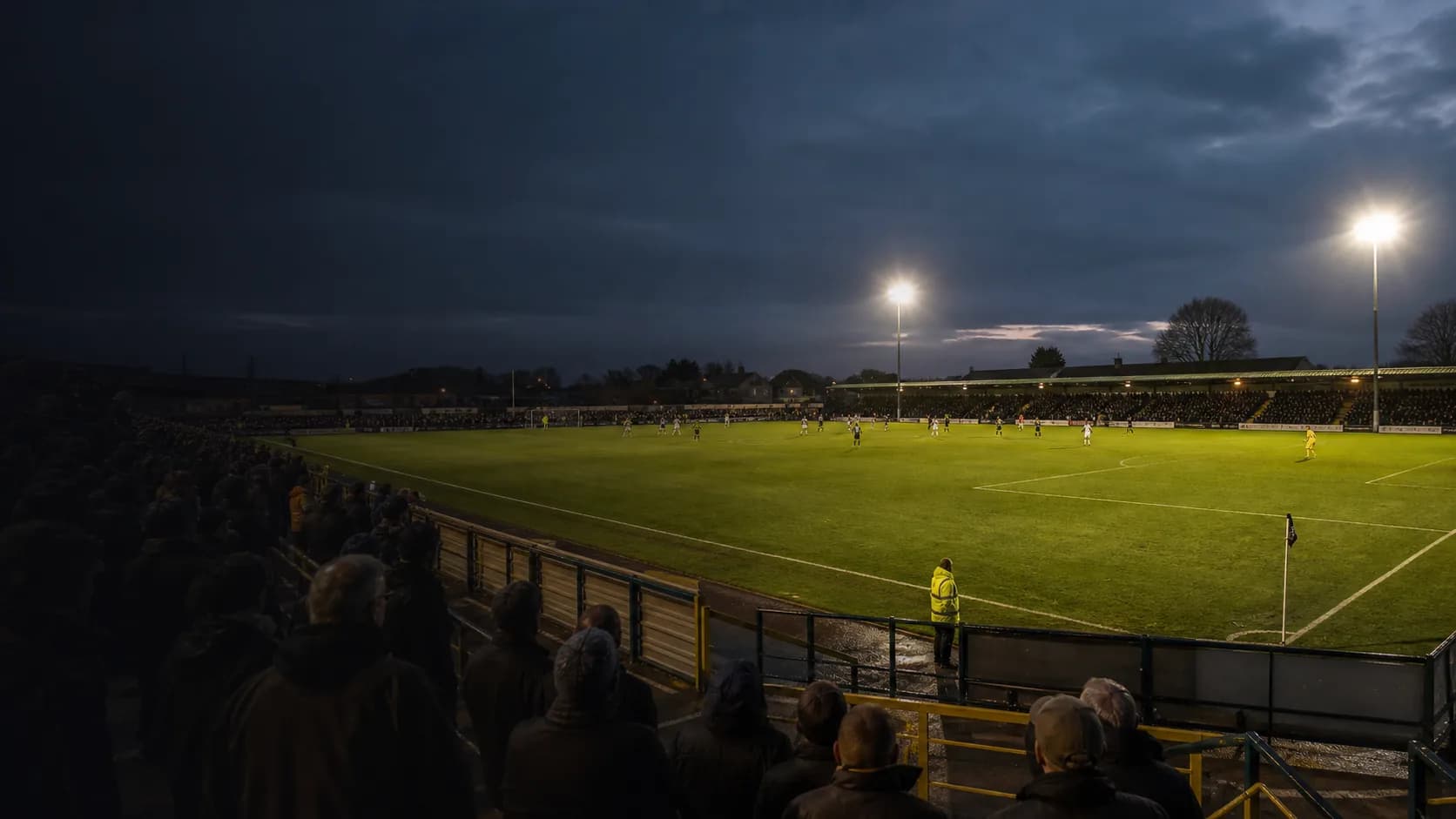 A compact football ground under evening floodlights